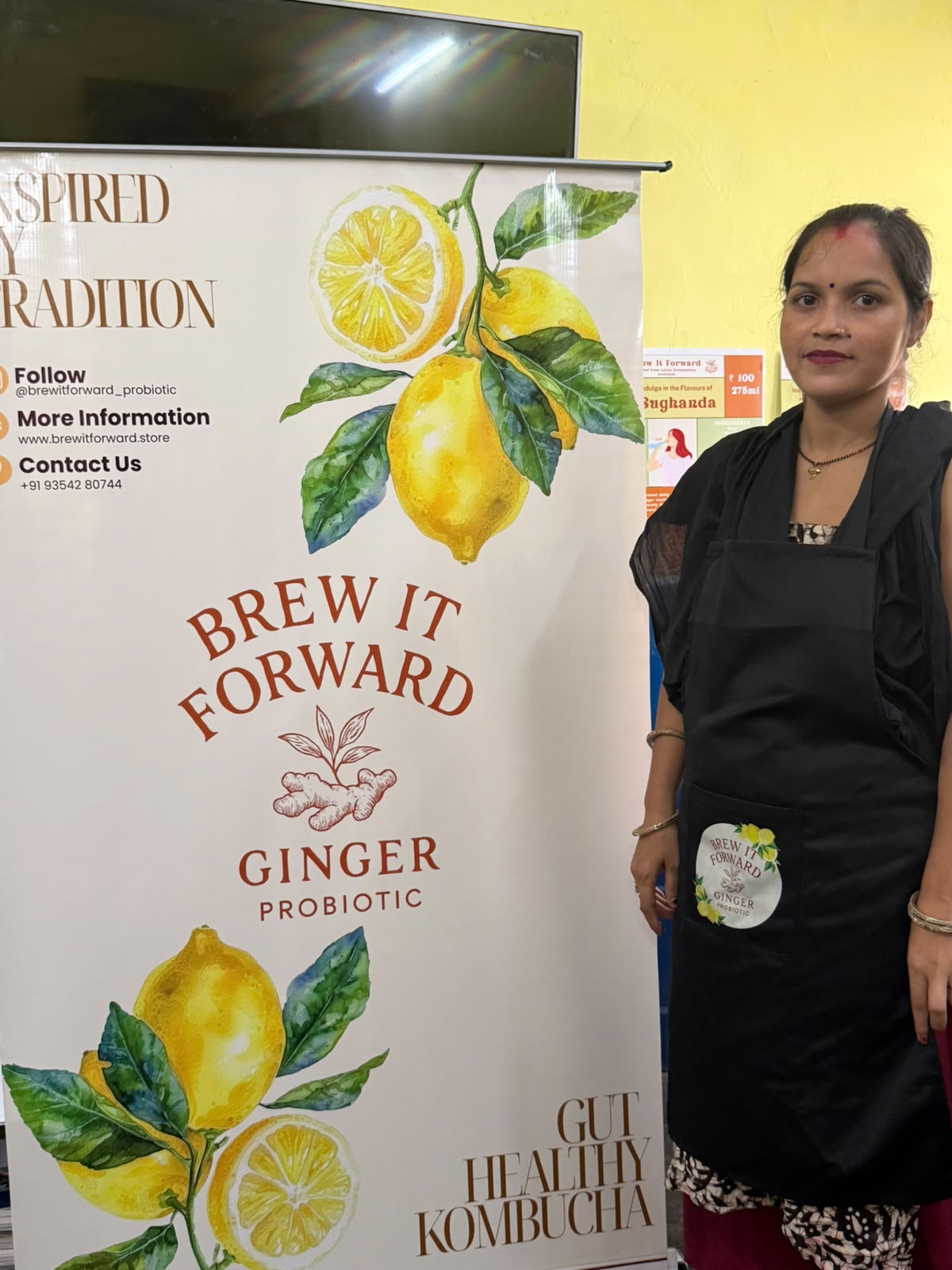 A woman participant standing beside the Brew It Forward banner